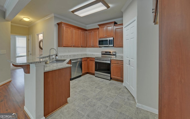 kitchen featuring stainless steel appliances, sink, light stone counters, kitchen peninsula, and a kitchen bar