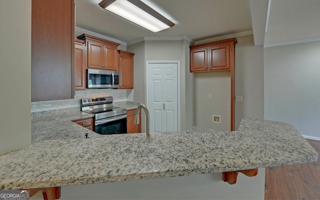 kitchen featuring stainless steel appliances, hardwood / wood-style flooring, kitchen peninsula, and ornamental molding