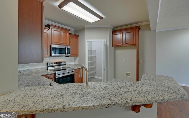 kitchen featuring ornamental molding, kitchen peninsula, appliances with stainless steel finishes, and wood-type flooring