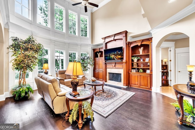 living room with ceiling fan, high vaulted ceiling, a high end fireplace, built in features, and dark hardwood / wood-style flooring