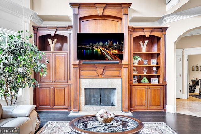 living room with built in features, a tiled fireplace, ornamental molding, and dark hardwood / wood-style floors