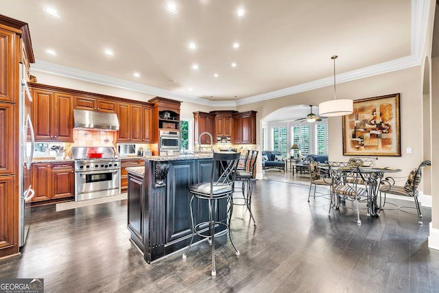 kitchen with stainless steel appliances, a breakfast bar, light stone counters, an island with sink, and pendant lighting