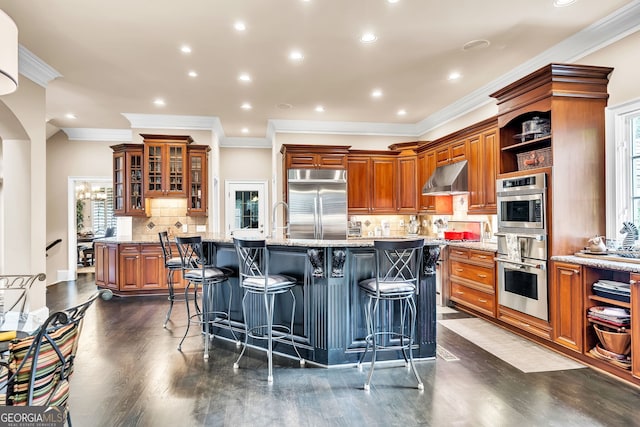 kitchen featuring light stone counters, appliances with stainless steel finishes, a kitchen breakfast bar, a kitchen island with sink, and dark hardwood / wood-style flooring