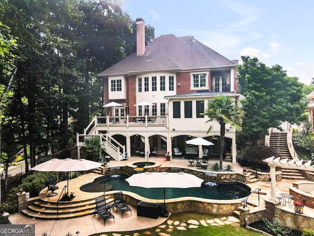 back of house with a swimming pool with hot tub, a patio, and a balcony