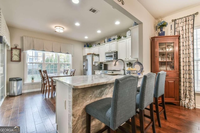 kitchen with a breakfast bar area, white cabinets, dark hardwood / wood-style floors, and stainless steel appliances