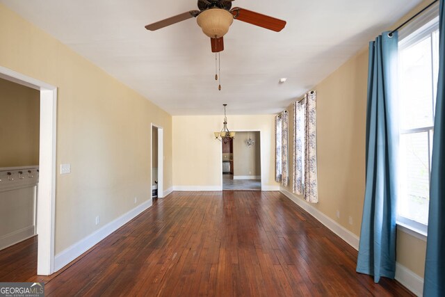 unfurnished room featuring ceiling fan with notable chandelier, dark wood-type flooring, and a healthy amount of sunlight