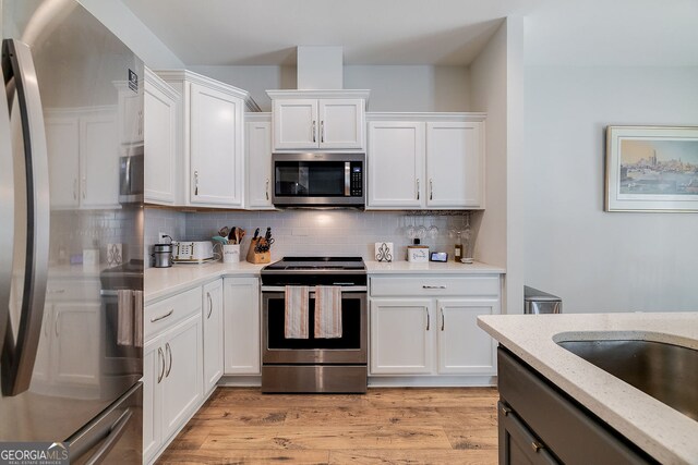 kitchen featuring stainless steel appliances, light hardwood / wood-style floors, light stone counters, white cabinets, and backsplash