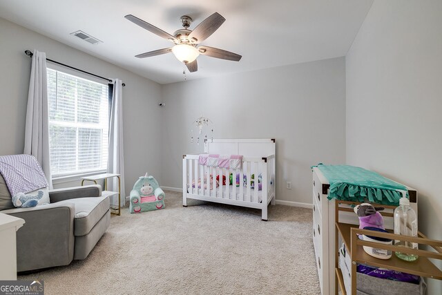 bedroom featuring light carpet, ceiling fan, and a crib