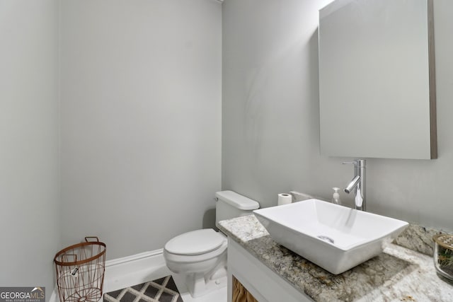 half bath featuring baseboards, vanity, and toilet