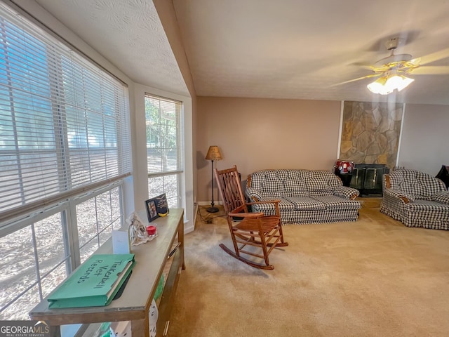 living room with a stone fireplace, a textured ceiling, ceiling fan, and carpet floors