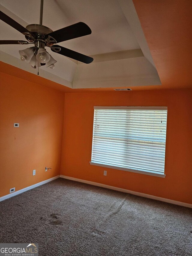 carpeted empty room with a tray ceiling, ceiling fan, and a healthy amount of sunlight