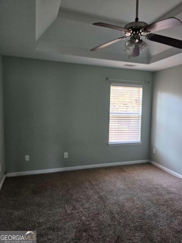 empty room featuring a raised ceiling, ceiling fan, and carpet floors