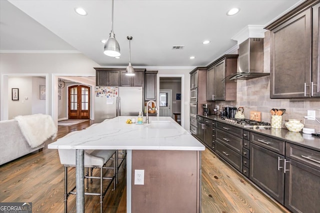 kitchen featuring hardwood / wood-style flooring, a center island with sink, sink, appliances with stainless steel finishes, and wall chimney exhaust hood