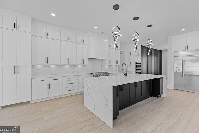 kitchen featuring stainless steel appliances, a large island with sink, light hardwood / wood-style flooring, white cabinetry, and hanging light fixtures