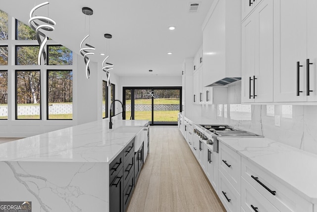 kitchen with a spacious island, light stone counters, hanging light fixtures, and light hardwood / wood-style floors