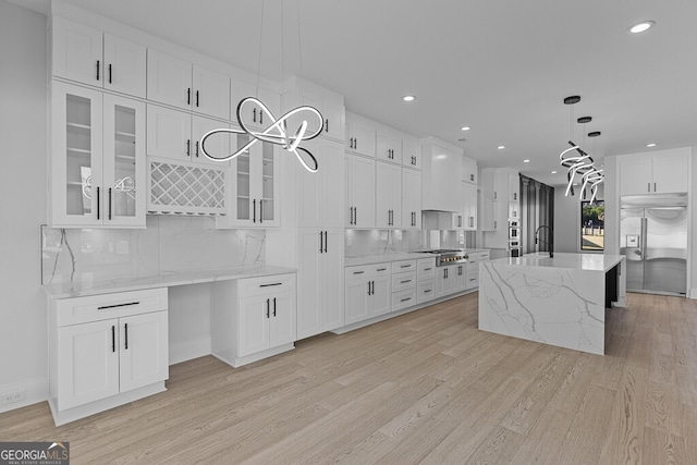 kitchen featuring white cabinetry, hanging light fixtures, an island with sink, light hardwood / wood-style floors, and appliances with stainless steel finishes