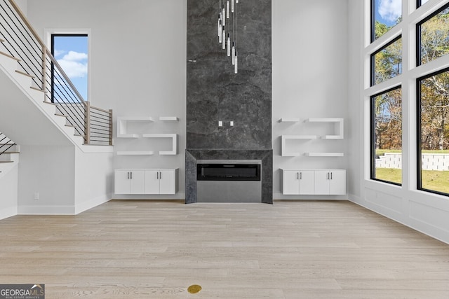 unfurnished living room with a wealth of natural light, a large fireplace, light hardwood / wood-style floors, and a high ceiling