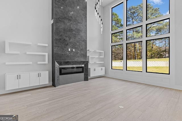 unfurnished living room with plenty of natural light, a large fireplace, a high ceiling, and light wood-type flooring