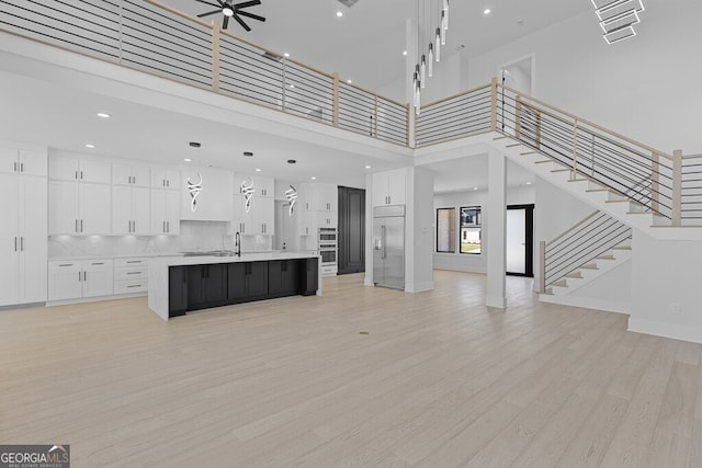 unfurnished living room featuring ceiling fan, light hardwood / wood-style floors, a towering ceiling, and sink