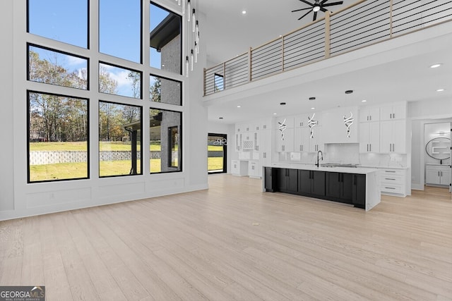 unfurnished living room featuring ceiling fan, light hardwood / wood-style flooring, and a towering ceiling