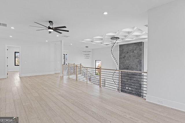 unfurnished living room featuring coffered ceiling, ceiling fan, beamed ceiling, and light hardwood / wood-style flooring