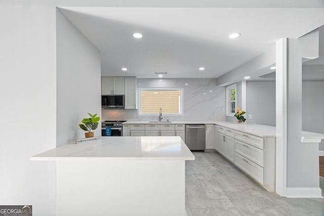 kitchen with appliances with stainless steel finishes, a peninsula, light countertops, a sink, and recessed lighting