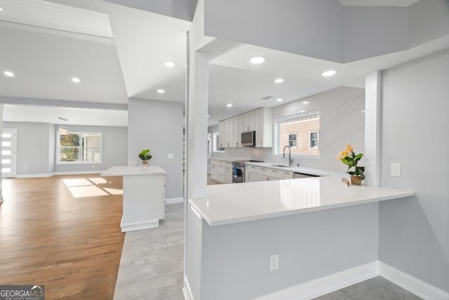 kitchen with light countertops, appliances with stainless steel finishes, open floor plan, a sink, and baseboards