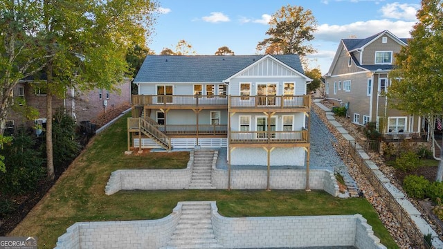 rear view of property with stairs, board and batten siding, a balcony, and a lawn