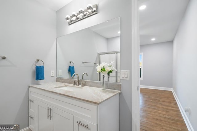 bathroom with recessed lighting, vanity, baseboards, and wood finished floors