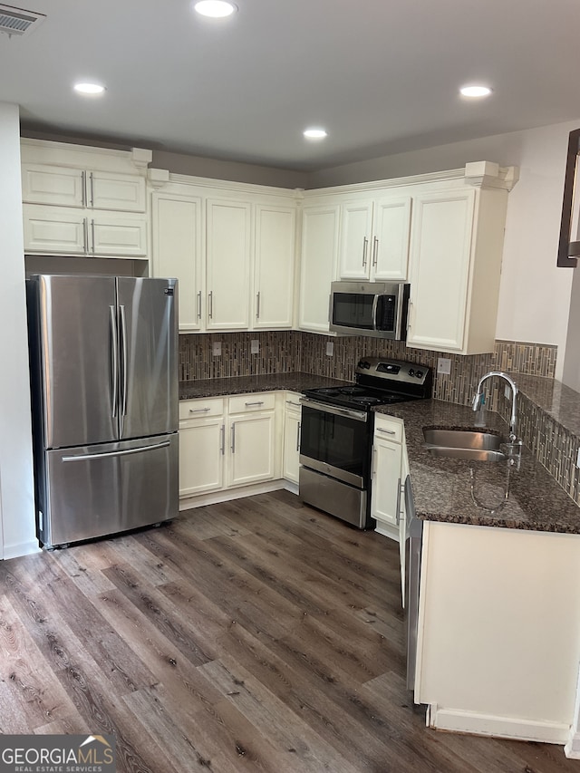 kitchen featuring sink, dark wood-type flooring, stainless steel appliances, backsplash, and dark stone counters