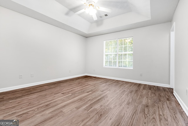 empty room with light hardwood / wood-style floors, ceiling fan, and a raised ceiling