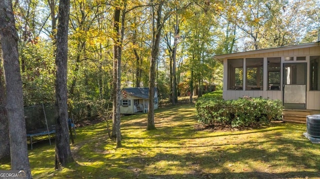 view of yard featuring central air condition unit, a sunroom, a trampoline, and an outdoor structure