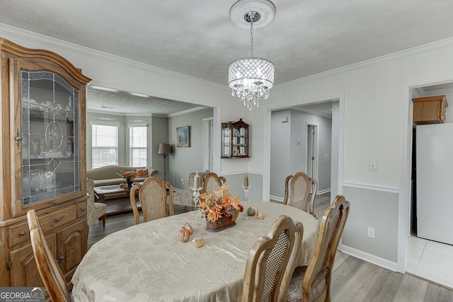 dining area featuring light hardwood / wood-style flooring, a textured ceiling, crown molding, and an inviting chandelier