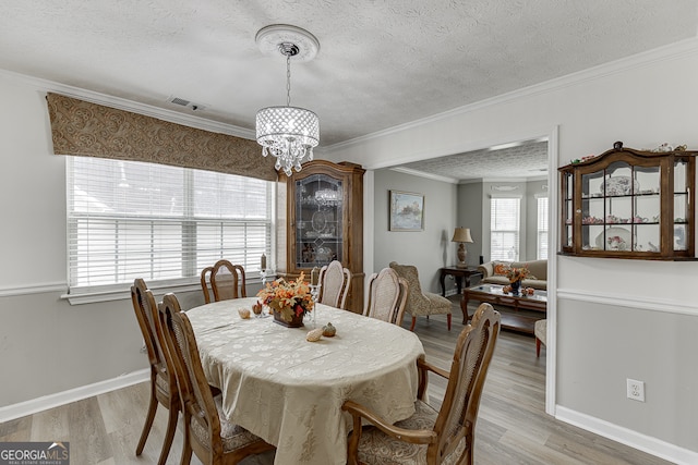 dining area with light hardwood / wood-style floors, a textured ceiling, crown molding, and an inviting chandelier