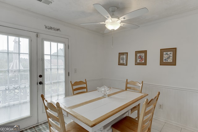 tiled dining space featuring wood walls, ceiling fan, a textured ceiling, and crown molding