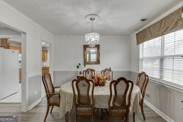 dining area with ornamental molding, light hardwood / wood-style flooring, a textured ceiling, and an inviting chandelier