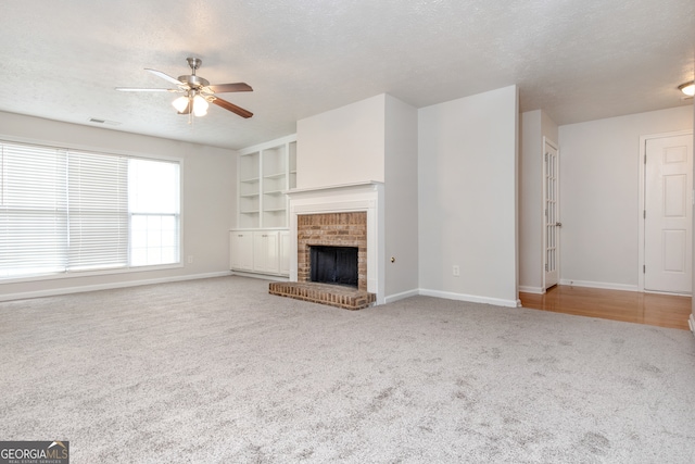 unfurnished living room featuring a textured ceiling, light carpet, ceiling fan, and a brick fireplace