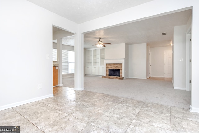 unfurnished living room featuring a brick fireplace, light colored carpet, a textured ceiling, ceiling fan, and built in features