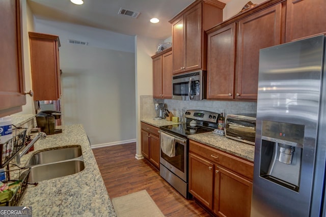 kitchen with light stone countertops, backsplash, stainless steel appliances, dark wood-type flooring, and sink