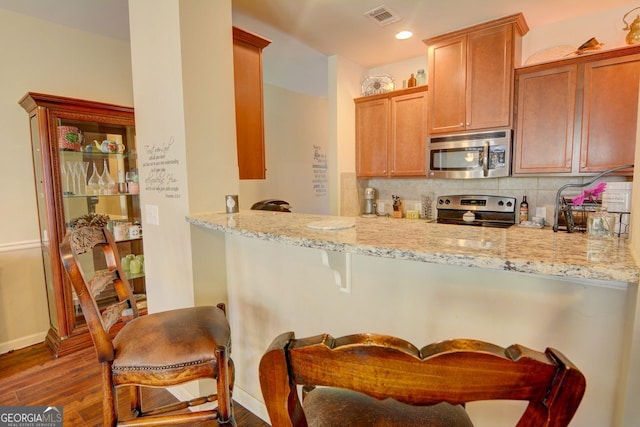 kitchen with dark hardwood / wood-style floors, light stone countertops, stainless steel appliances, and a breakfast bar area