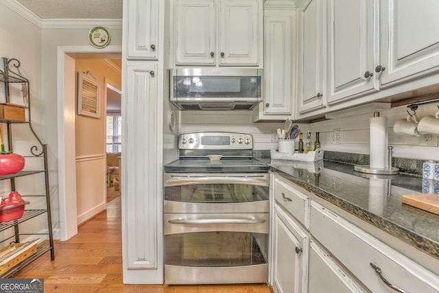 kitchen with white cabinets, dark stone countertops, stainless steel appliances, crown molding, and light wood-style floors