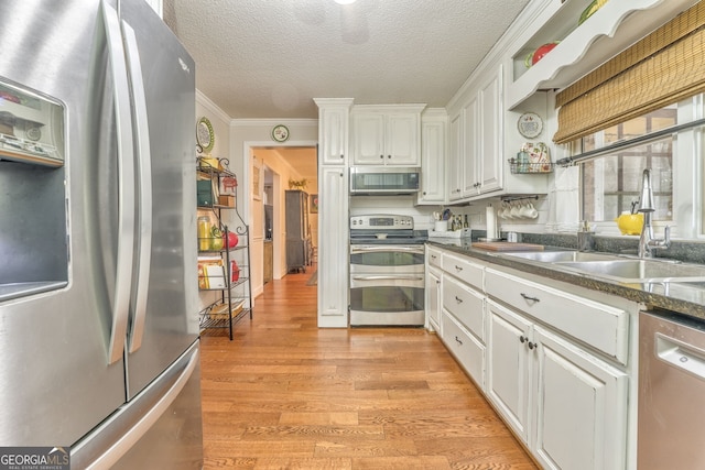 kitchen with a sink, light wood-style floors, white cabinets, ornamental molding, and appliances with stainless steel finishes