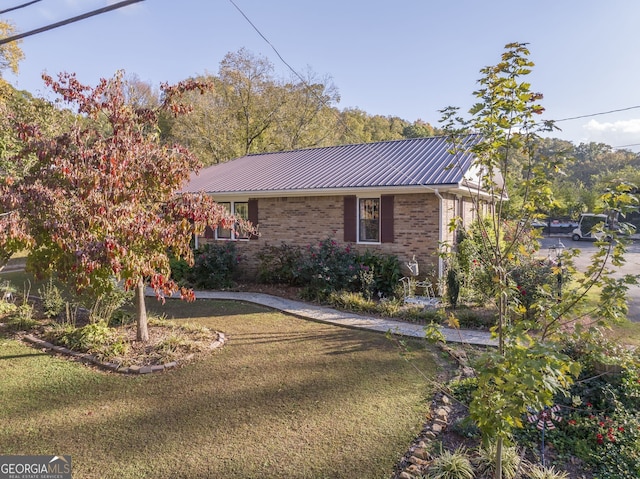 single story home with a front yard, brick siding, and metal roof