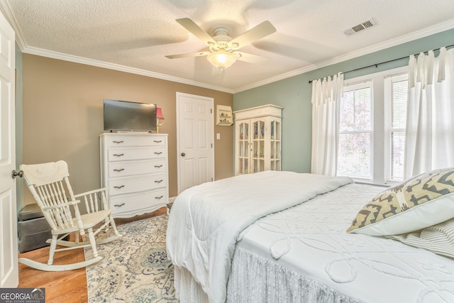 bedroom featuring light wood-style floors, a textured ceiling, visible vents, and crown molding