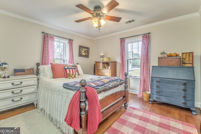 bedroom featuring a textured ceiling, ornamental molding, wood finished floors, and visible vents