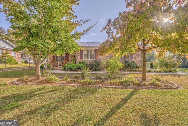 view of property hidden behind natural elements with brick siding, metal roof, and a front yard