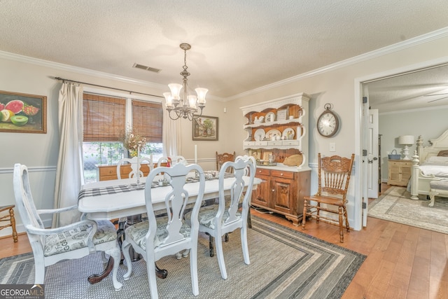 dining room with visible vents, hardwood / wood-style floors, crown molding, a textured ceiling, and a chandelier