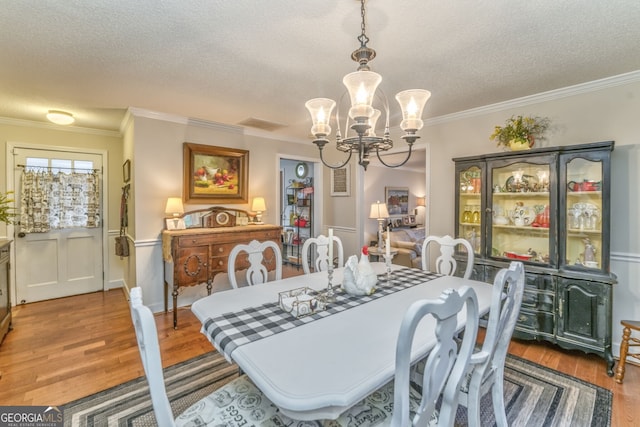 dining area with a textured ceiling, ornamental molding, wood finished floors, and a notable chandelier