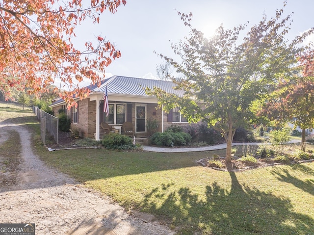 view of front of home with brick siding, dirt driveway, a standing seam roof, metal roof, and a front lawn