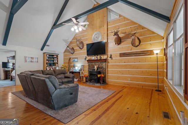 living room featuring a wood stove, hardwood / wood-style floors, high vaulted ceiling, beamed ceiling, and ceiling fan